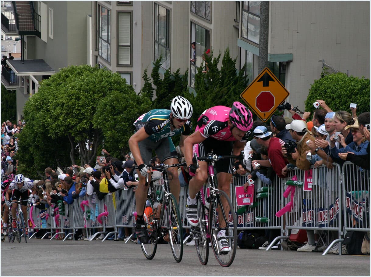 Jason Lokkesmoe in a breakaway at the San Francisco Grand Prix 2003, cresting a hill alongside a T-Mobile professional rider with large crowds watching