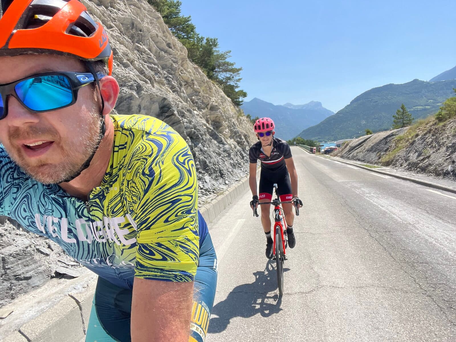 Jason and Olen Lokkesmoe cycling together on a mountain road with dramatic alpine scenery